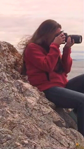Alex, in her natural habitat, atop a rock with something watery in her viewfinder. Photo by Michael Stillwater.